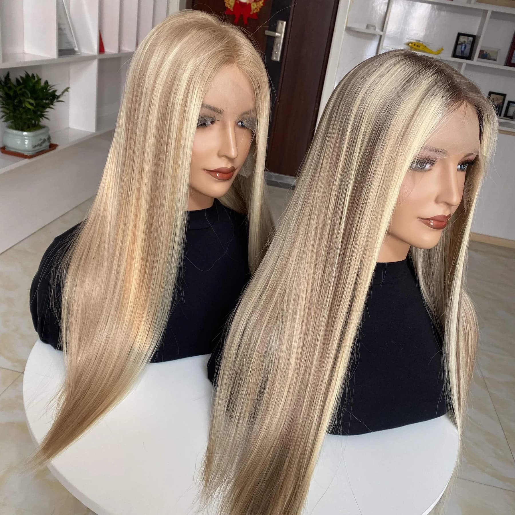 Two mannequin heads wearing long straight blonde wigs with different root colors and visible untrimmed front lace