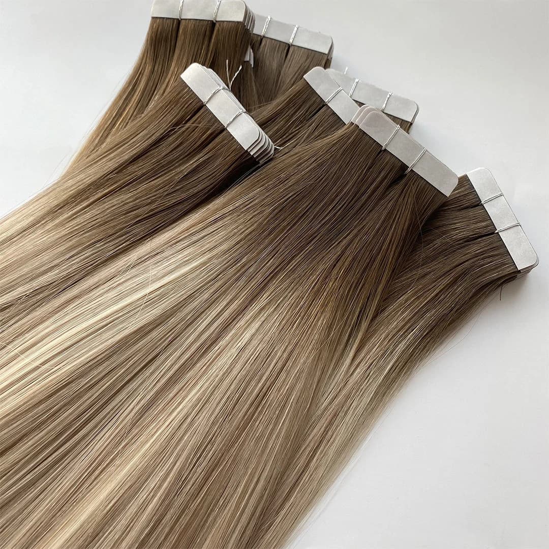 Rooted brown-to-blonde tape-in extension bundles with white protective liners over the attachment tabs