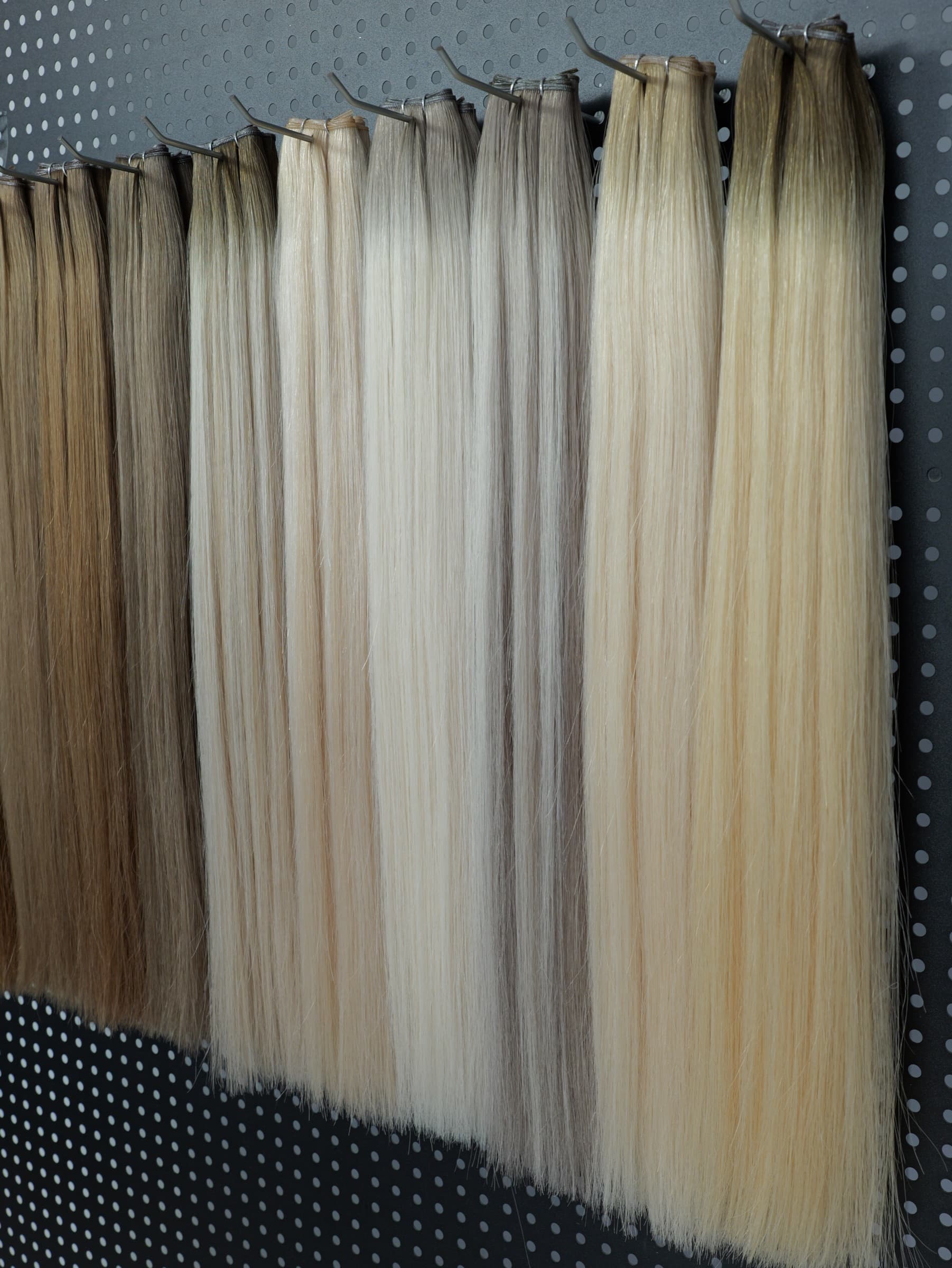Human hair extension shade swatches ranging from brunette to blonde on a display wall