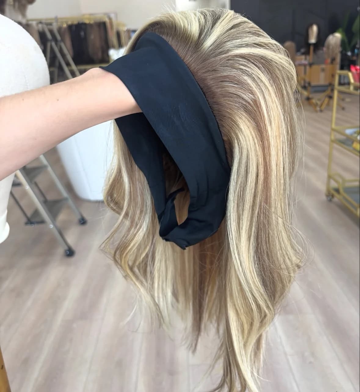 Highlighted wig held from the front with a wide black headband and brown-to-blonde lengths