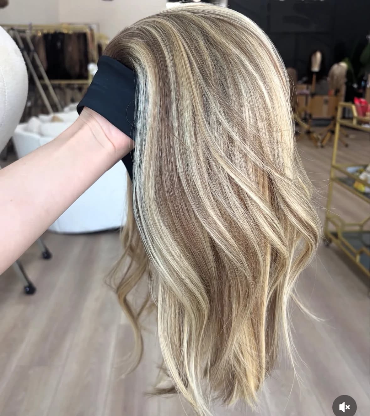 Hand-held side view of a highlighted brown and blonde wig with loose bends through the lengths
