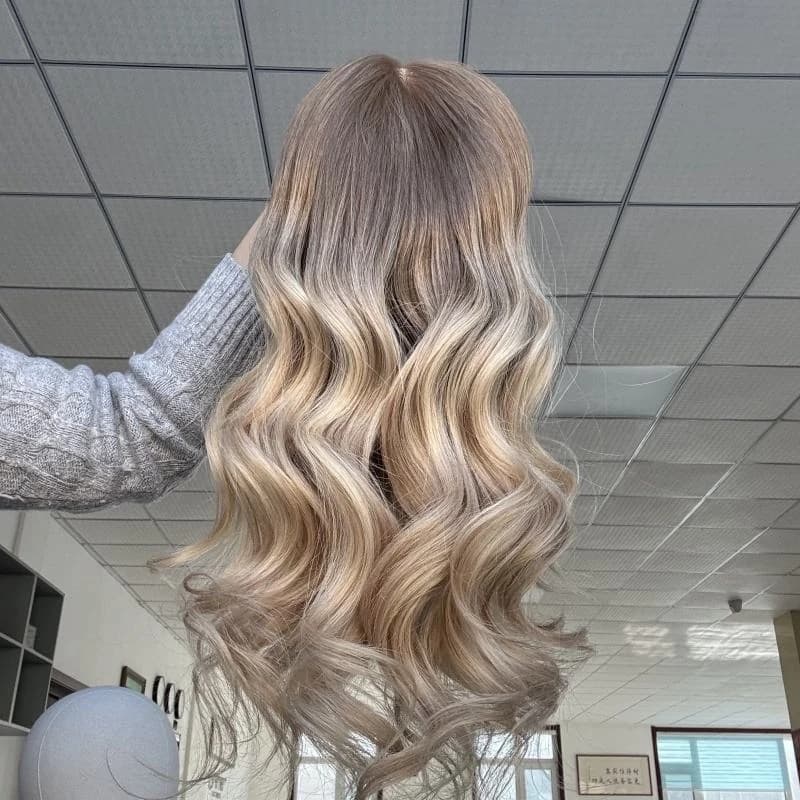 Long rooted blonde wavy wig held up to show its crown, blended color and styled lengths