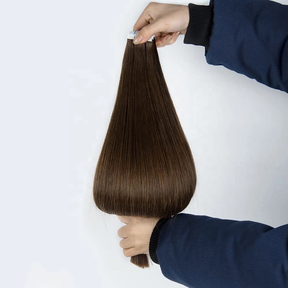 Hands holding dark brown straight tape-in hair extensions with the attachment tabs visible at the top
