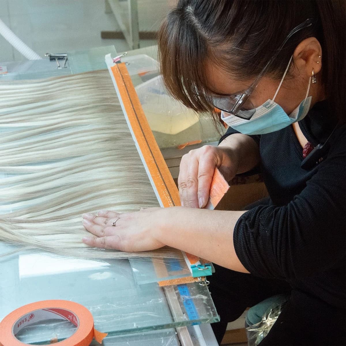 Technician arranging light-colored hair on a glass workbench beside an orange guide strip