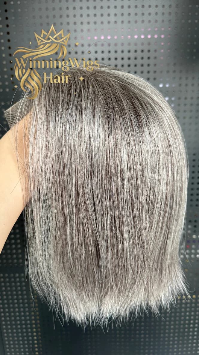 Gray bob-length hairpiece held up against a perforated display background with a WinningWigs watermark